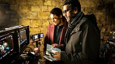 Detective Harry Virdee discussing a case with a colleague inside a dimly lit room in BBC’s Virdee.